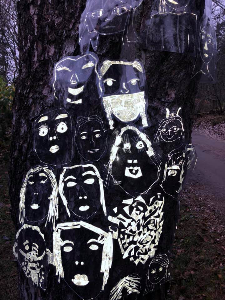 Kirkkonummen kuvataidekoulun oppilaiden heijastinkankaasta tekemiä kasvoja puun rungossa.