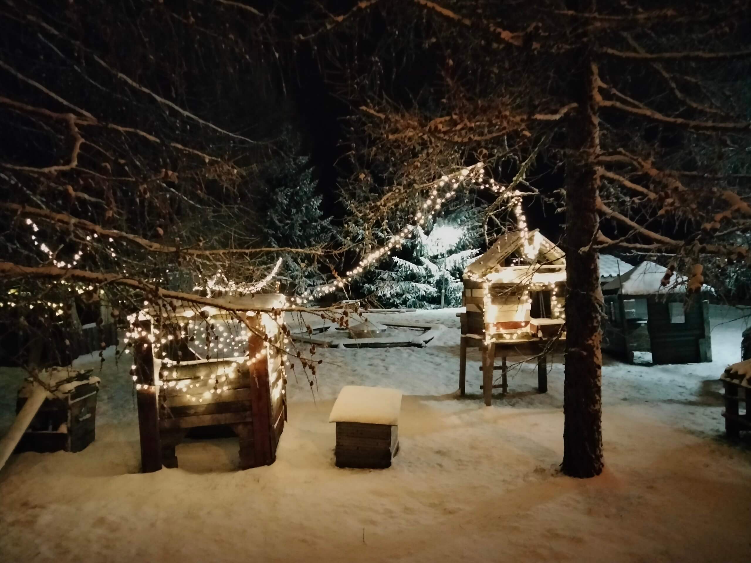 Valaistuja puusta rakenettuja majoja lumisessa maisemassa.