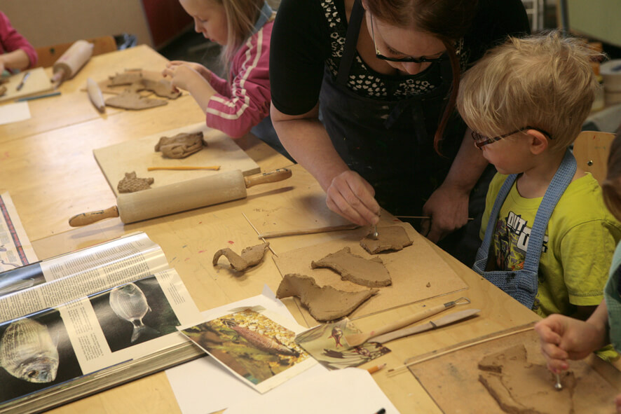Lapsia tekemässä keramiikkaa opettajan opastuksella.