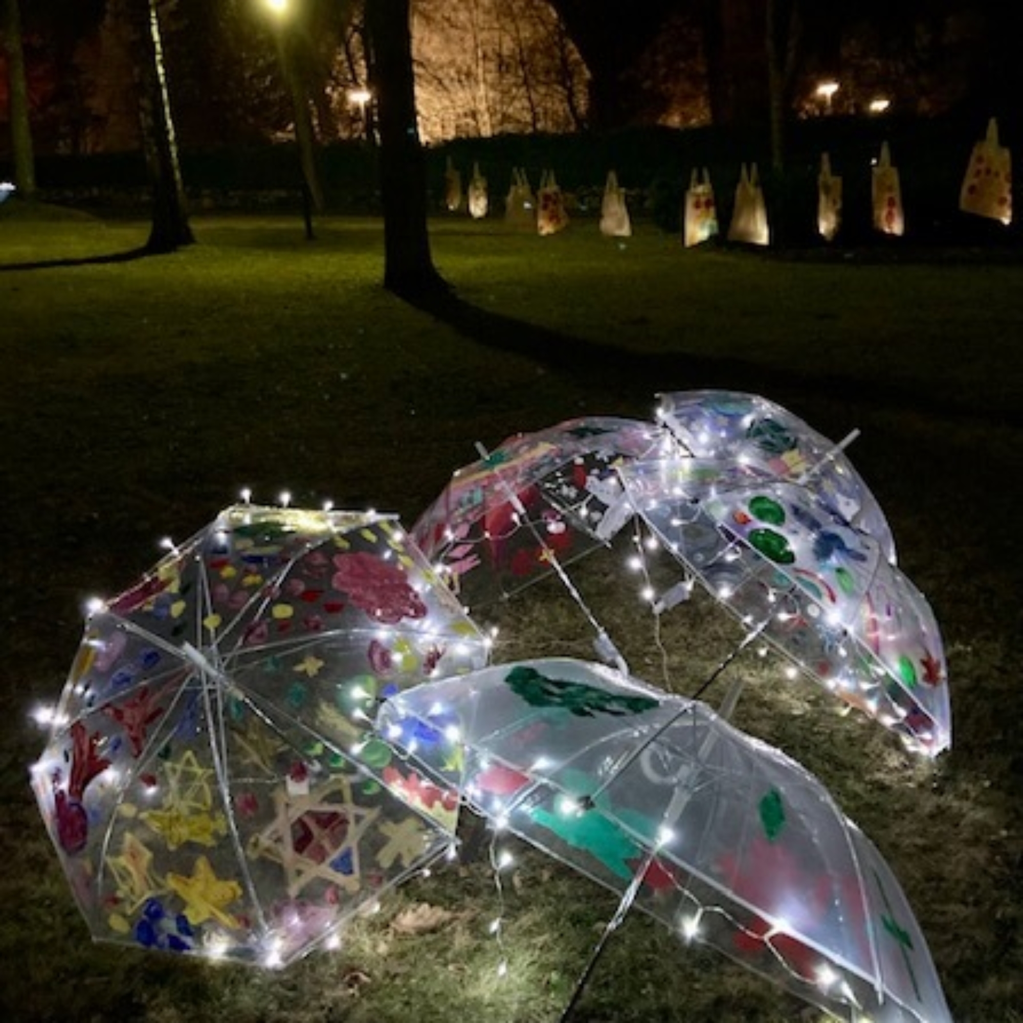 Valonauhalla valaistuja, lasten maalaamia läpinäkyvästä muovista valmistettuja sateenvarjoja nuormikolla.