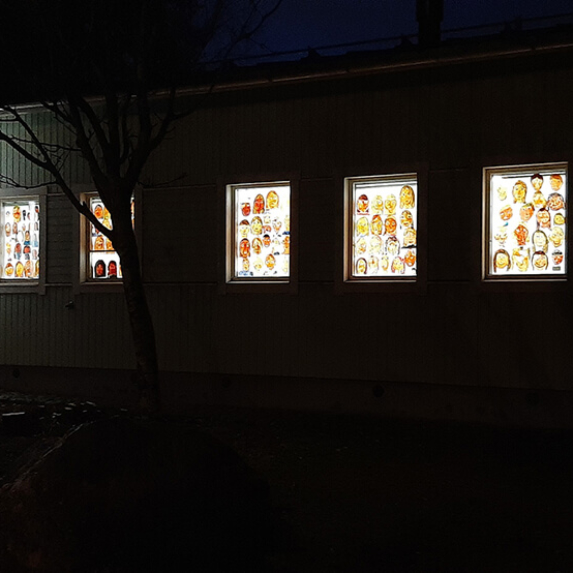 Lasten maalaamia omakuvia puutalon ikkunoissa pimeässä illassa.