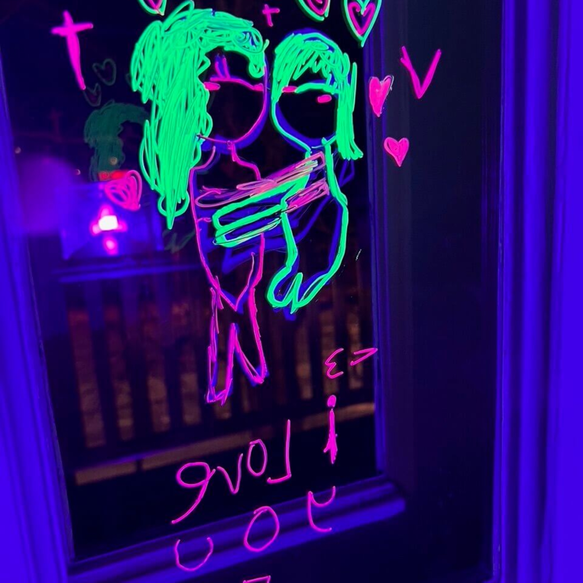UV-valossa loistava halaavaa pariskuntaa ja sydämiä esittävä piirustus ikkunassa.