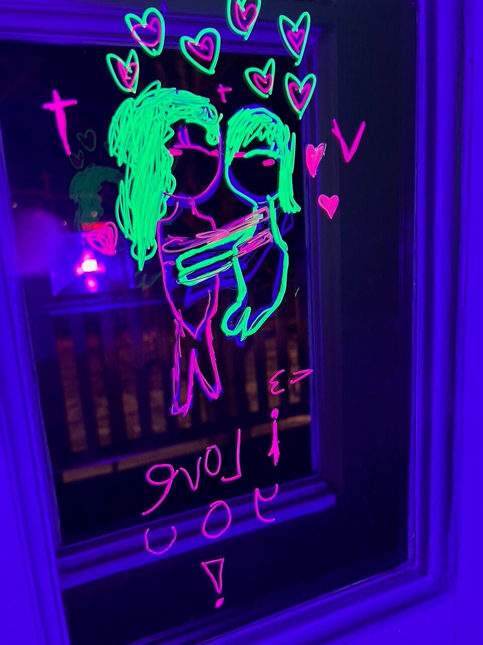 UV-valossa loistava halaavaa pariskuntaa ja sydämiä esittävä piirustus ikkunassa.