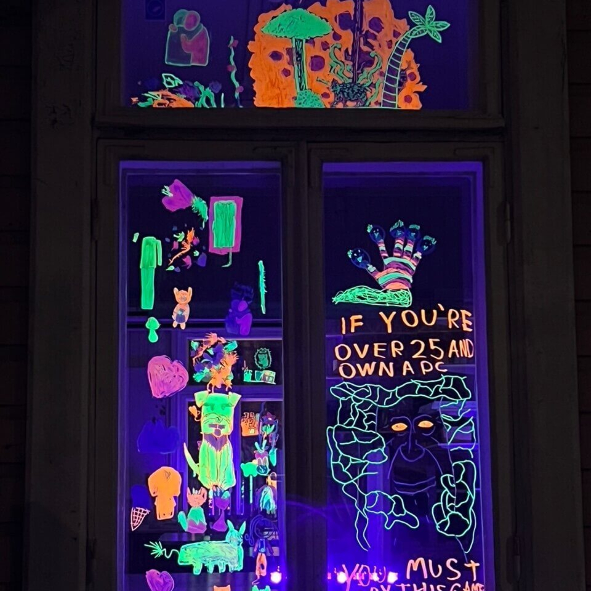 UV-valossa loistavia värikkäitä lasten piirroksia ja tekstejä ikkunassa.