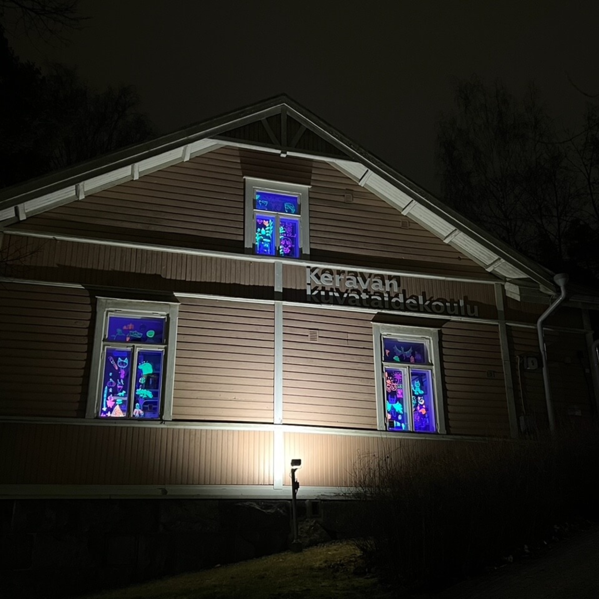 UV-valolla valaistuja värikkäitä piirroksia Keravan kuvataidekoulun ikkunoissa.