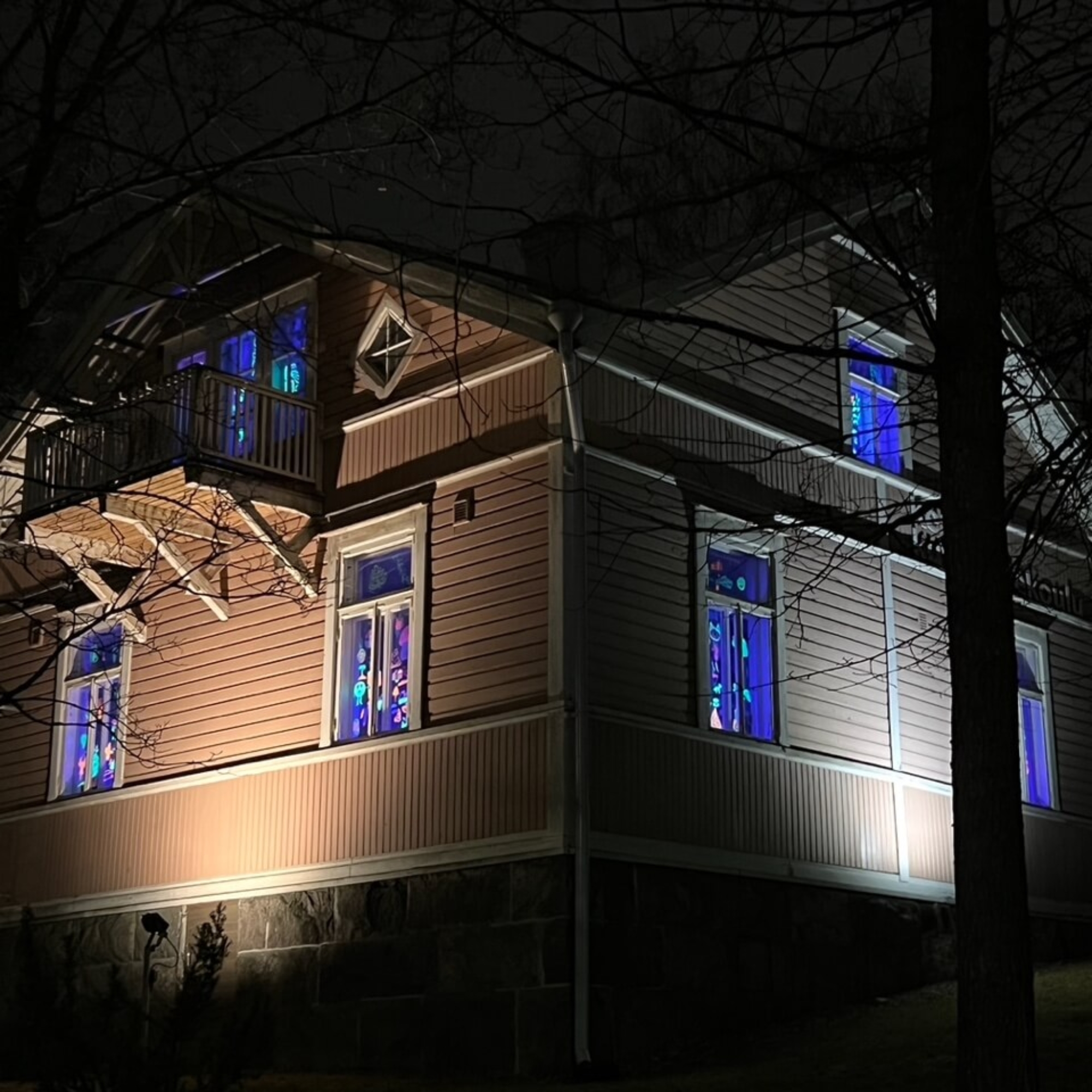 Ruskea puutalo, jonka ikkunoissa loistaa uv-valolla valaistuja värikkäitä piirustuksia.
