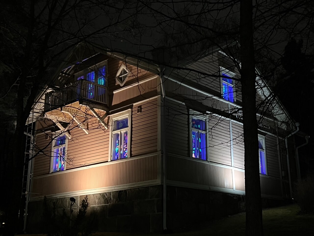Ruskea puutalo, jonka ikkunoissa loistaa uv-valolla valaistuja värikkäitä piirustuksia.