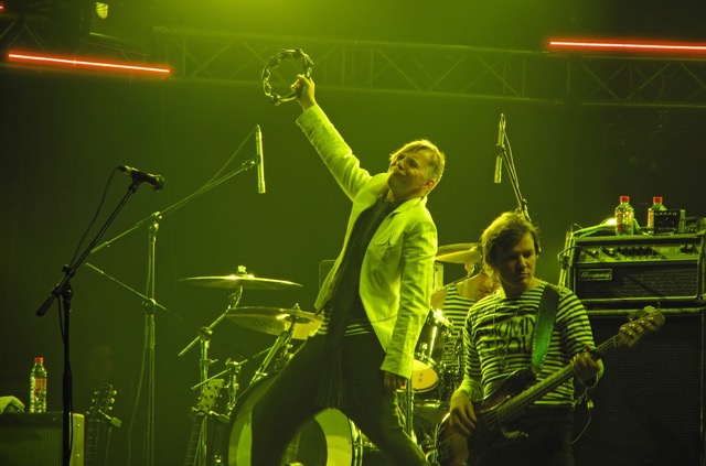 Basisti ja tamburiinin soittaja lavalla vihreässä valaistuksessa.