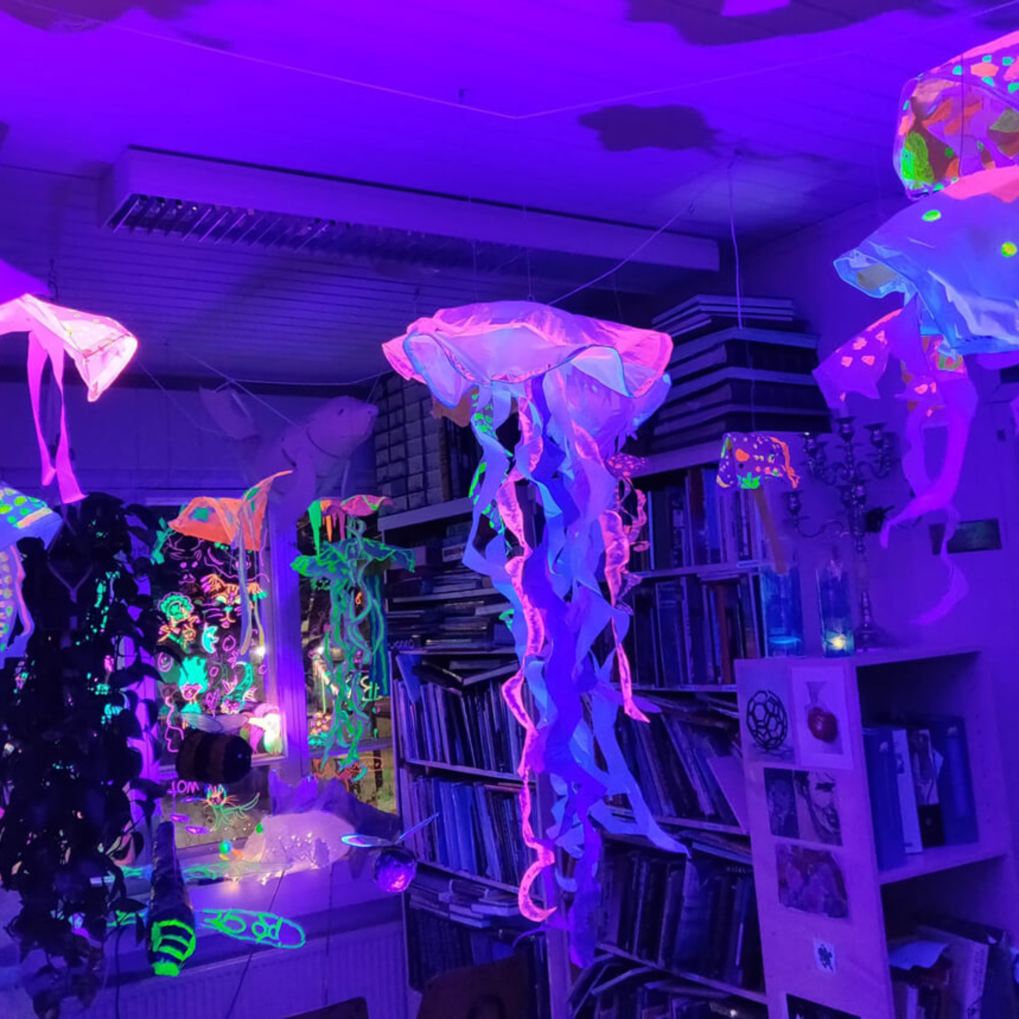 Uv-valolla valaistuja paperisia meduusan näköisiä teoksia roikkumassa huoneen katosta.