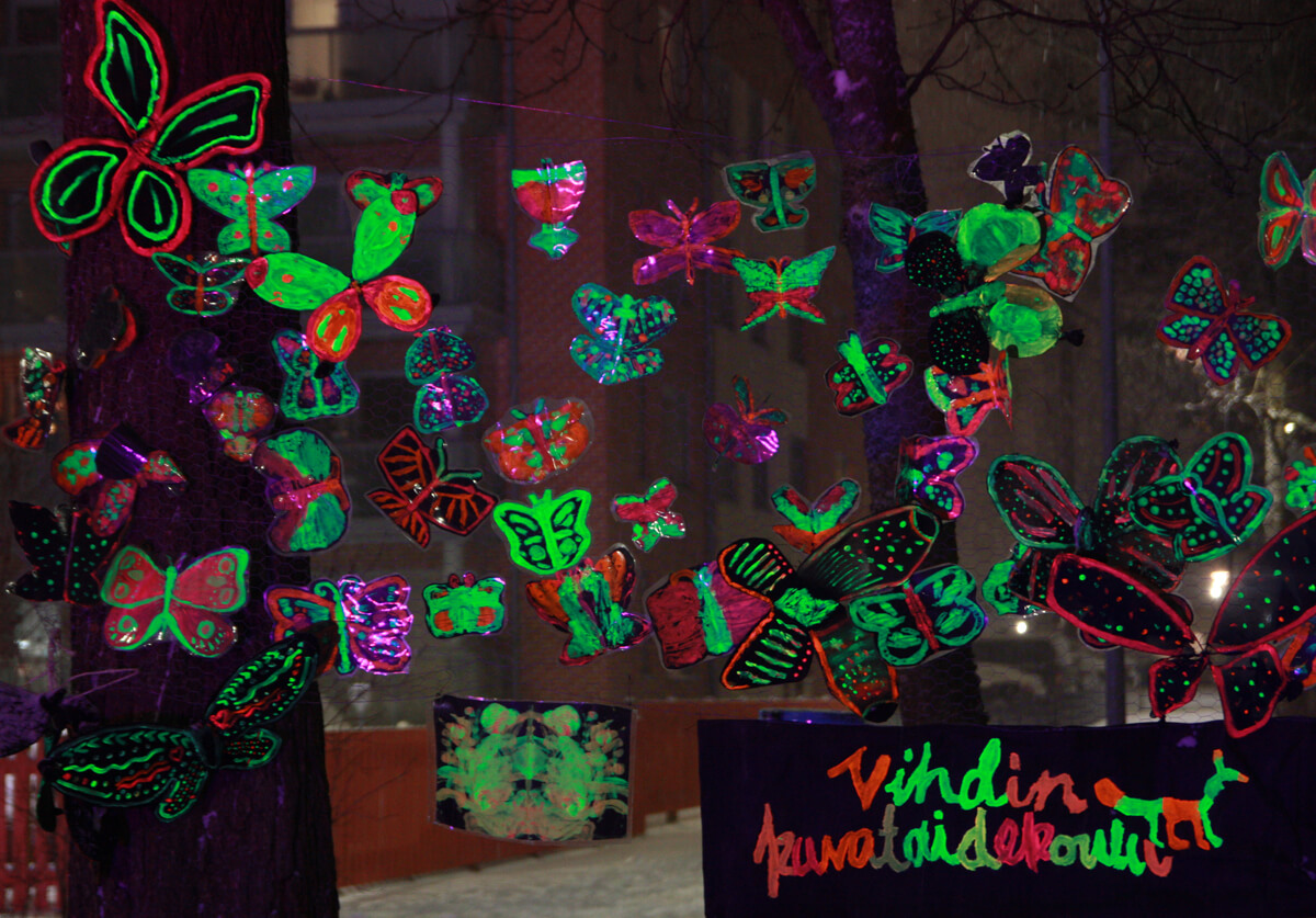 Uv-valolla valaistuja värikkäitä maalattuja perhosia ja teksti, jossa lukee Vihdin kuvataidekoulu.