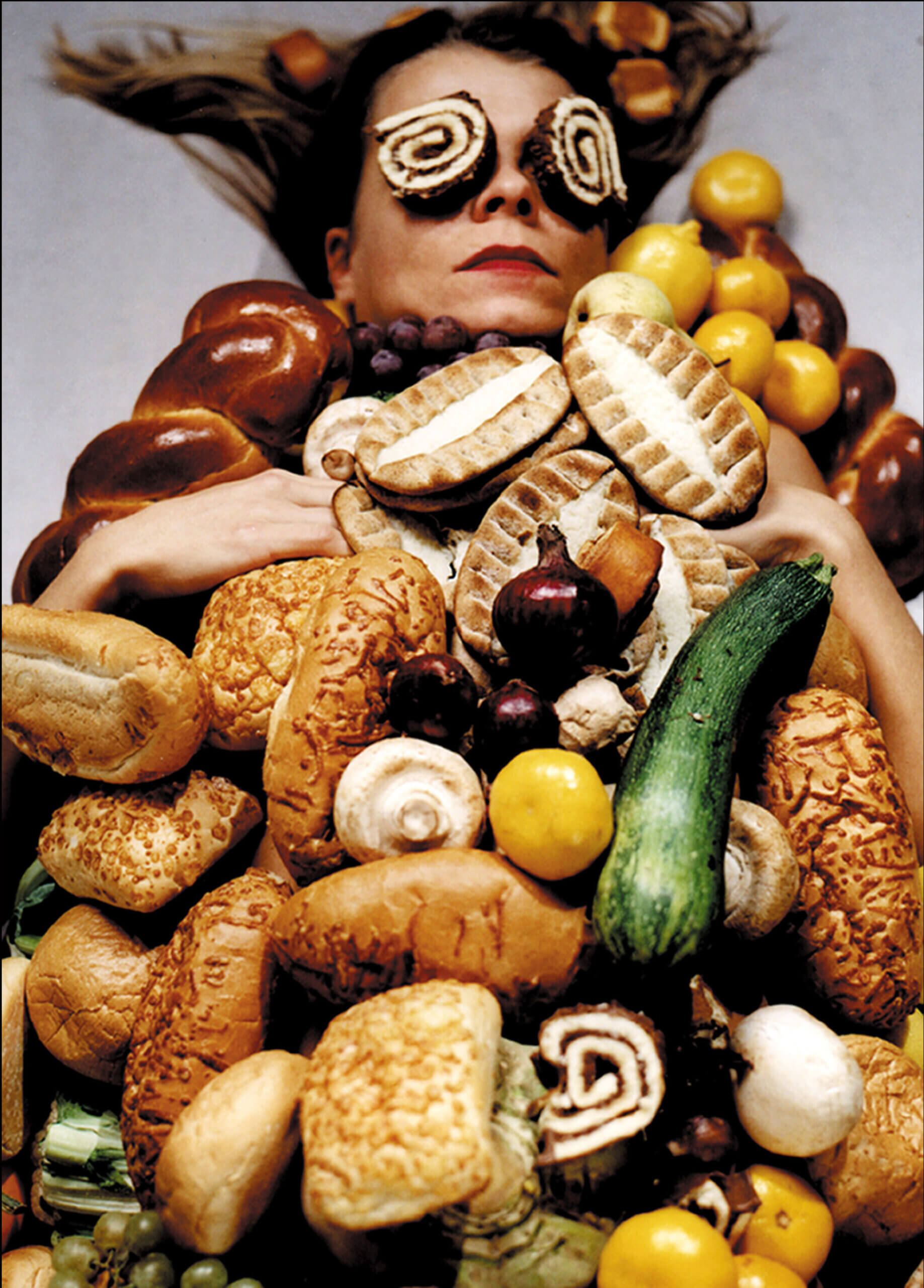 VAlokuvateos, jossa näkyy naisen kasvot vihannesten ja juuresten alta.